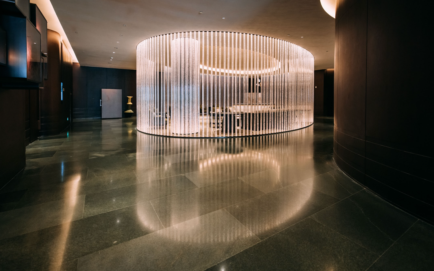 A modern lobby with a curved light installation reflecting on a dark, glossy floor.