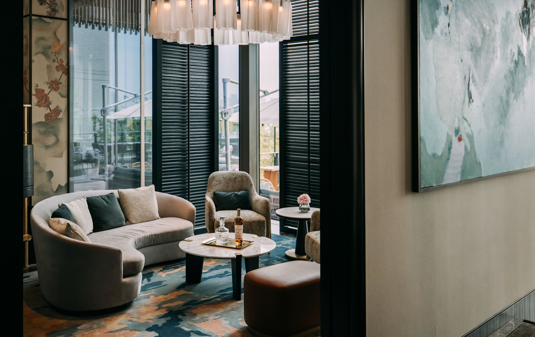 Cozy lounge with curved sofa, armchairs, and round coffee table. Large windows with shutters.