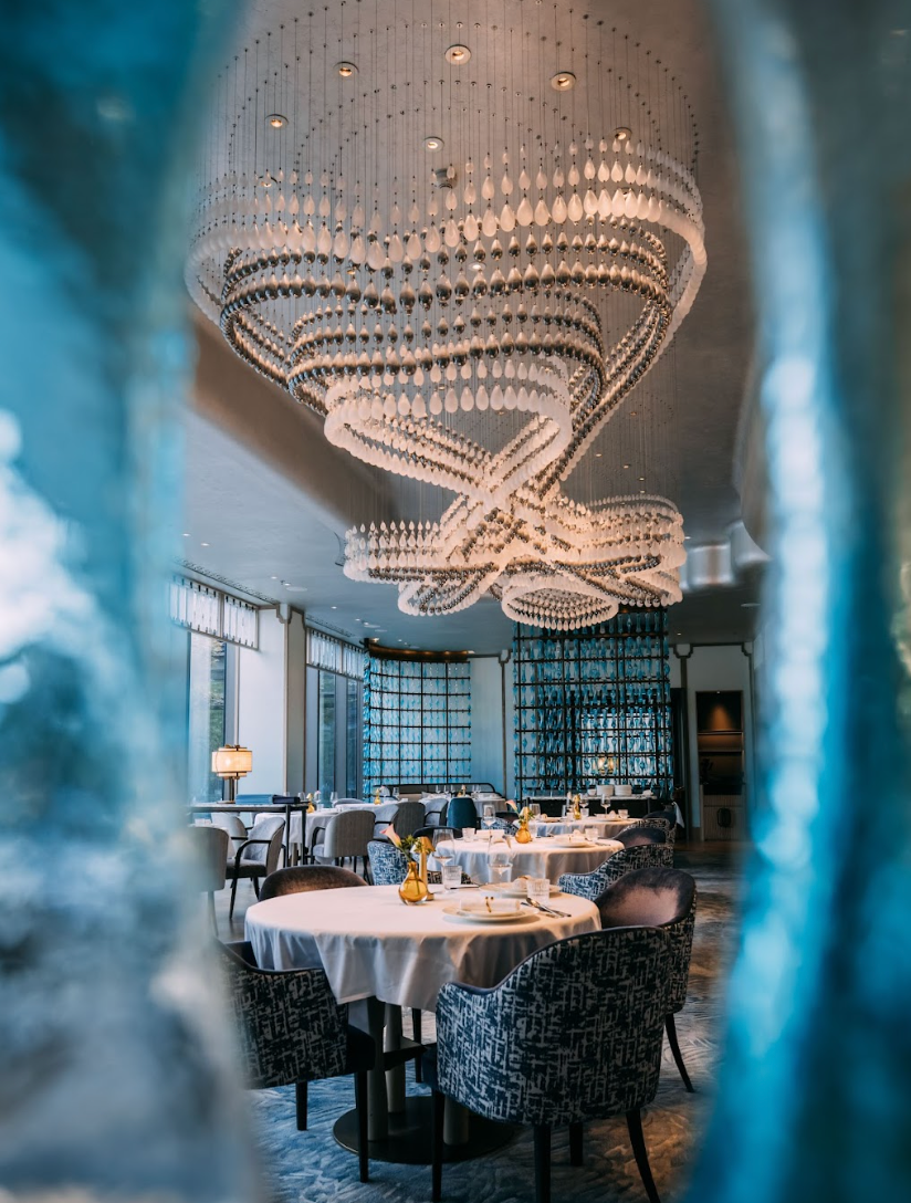 Elegant restaurant interior with round tables, patterned chairs, and a large chandelier.
