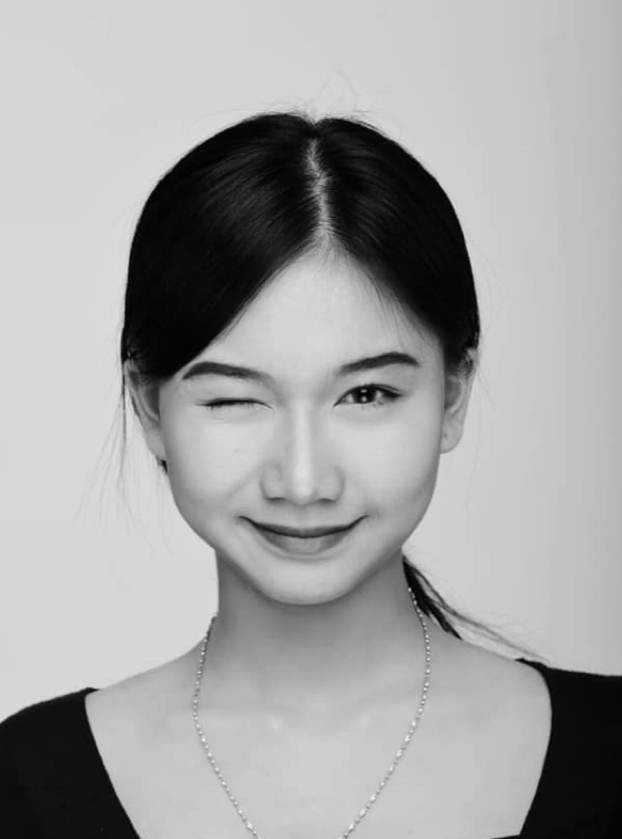 Woman winking, wearing a black top and a cross necklace, against a white background.