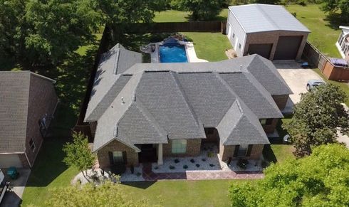 Aerial view of a gray-roofed house with a backyard pool and detached garage surrounded by green lawn.