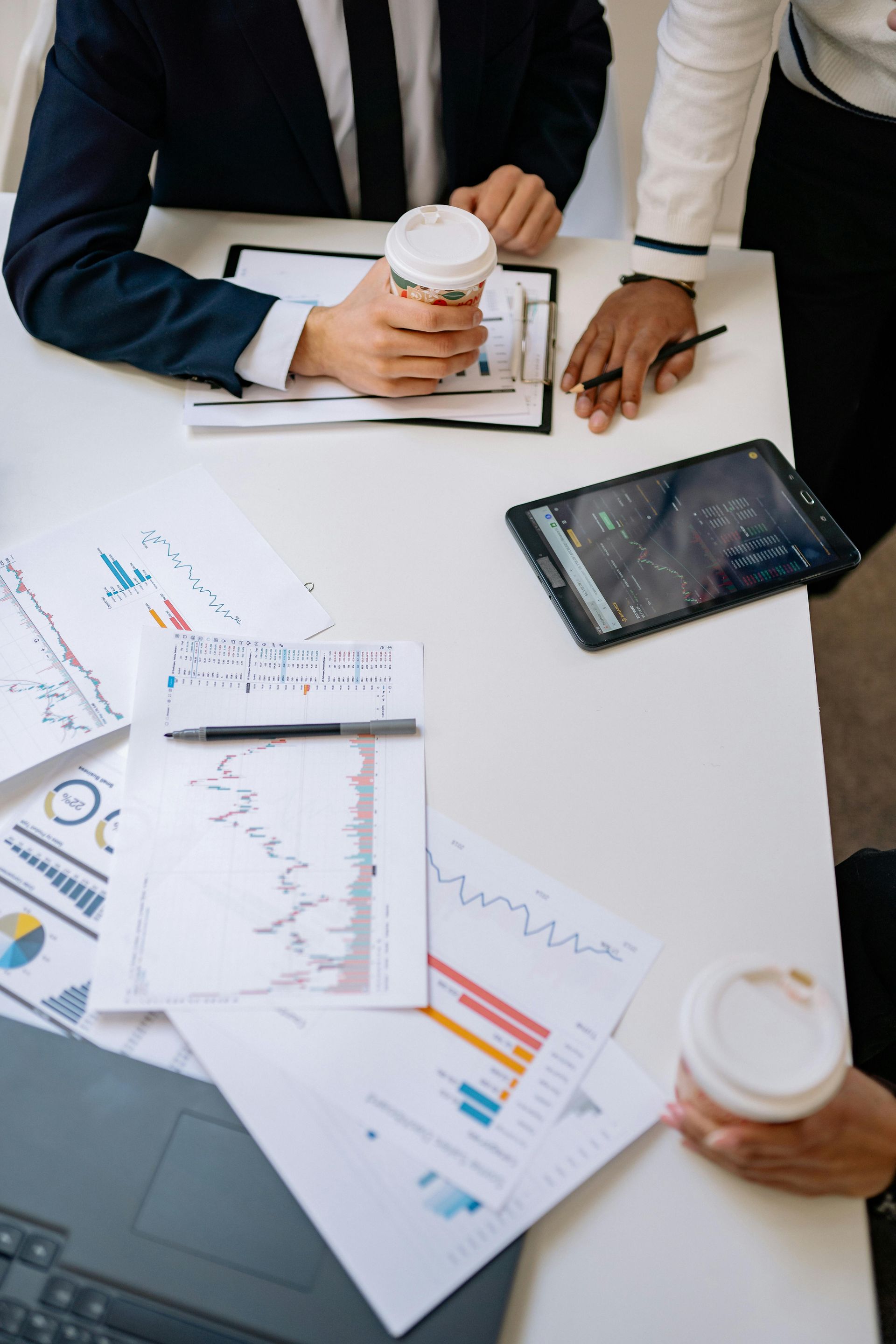 Team reviewing printed charts at a white table with coffee cups and a tablet.