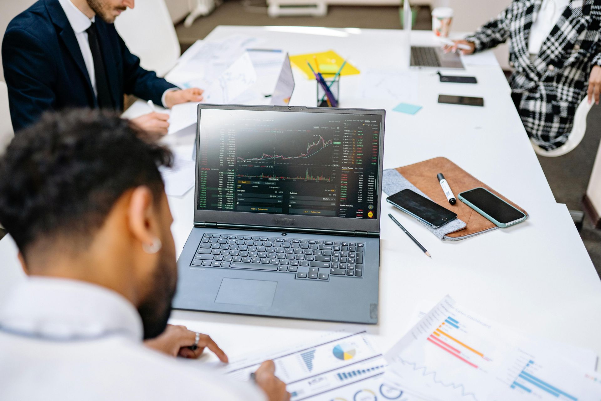 Team meeting around a laptop showing charts in a bright office, with notebooks and phones on the table.