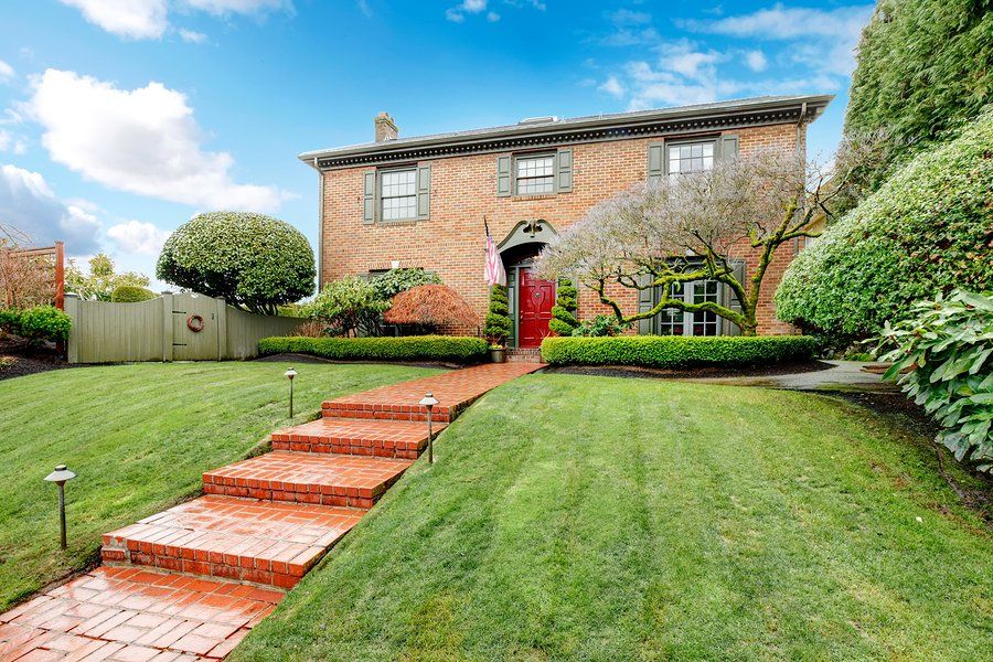 Brick house in Yorba Linda with large windows and exterior shutters red wood door stoned walkway trim hedge exotic trees