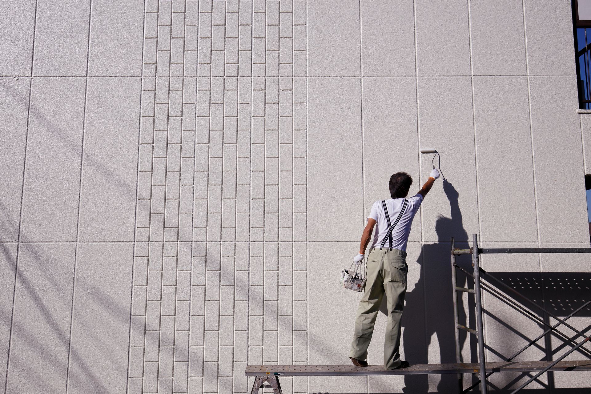 Commercial painter using a roller to paint the exterior wall of a building on scaffolding