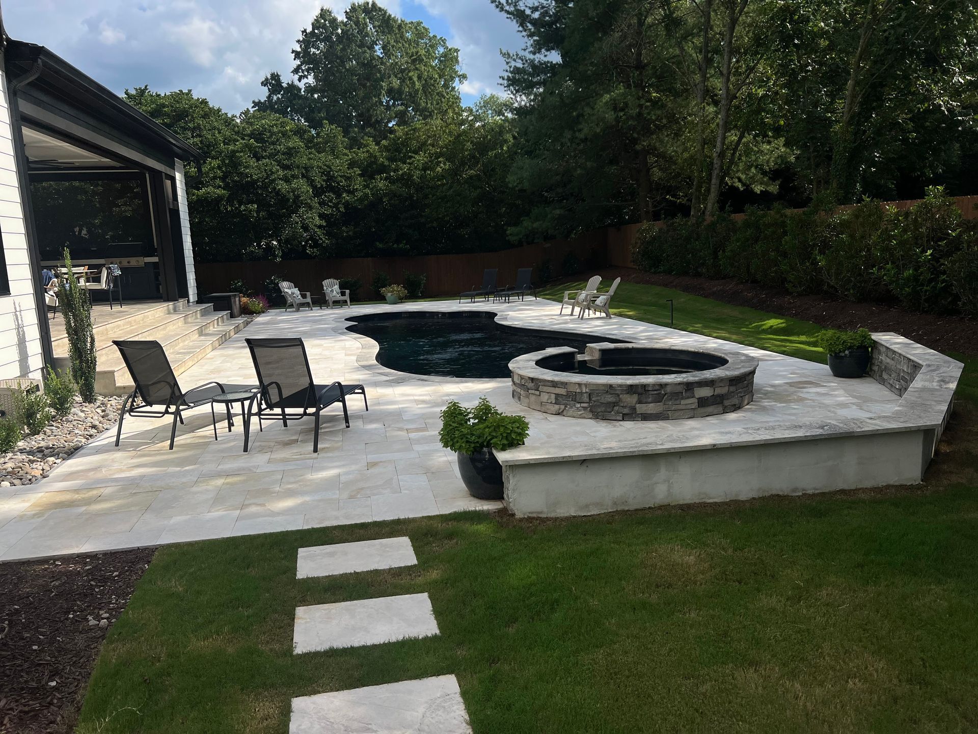 Backyard patio with curved stone fire pit, lounge chairs, and stepping stones on a lawn