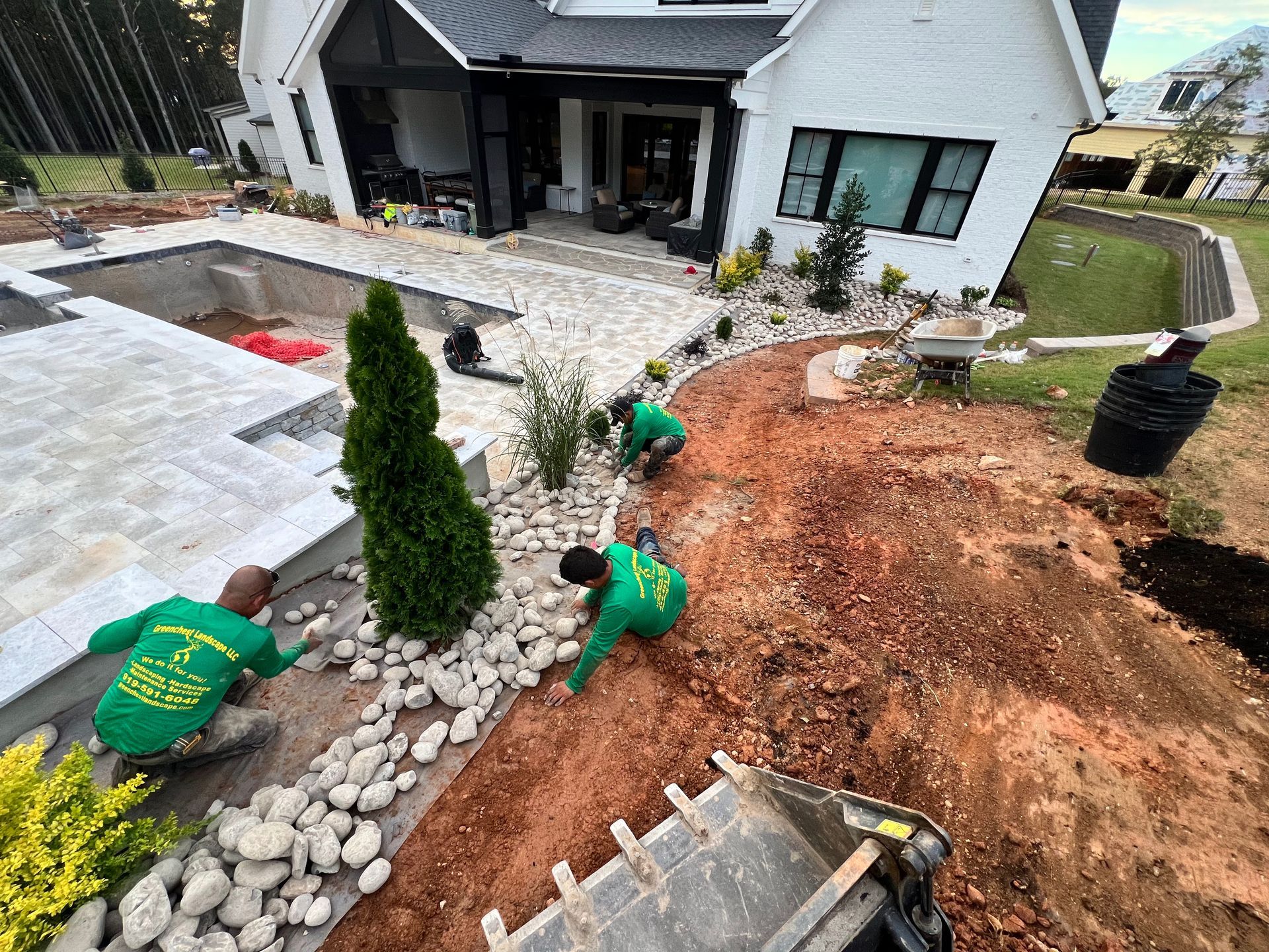 Landscaped front yard with workers planting shrubs beside a white house and stone walkway
