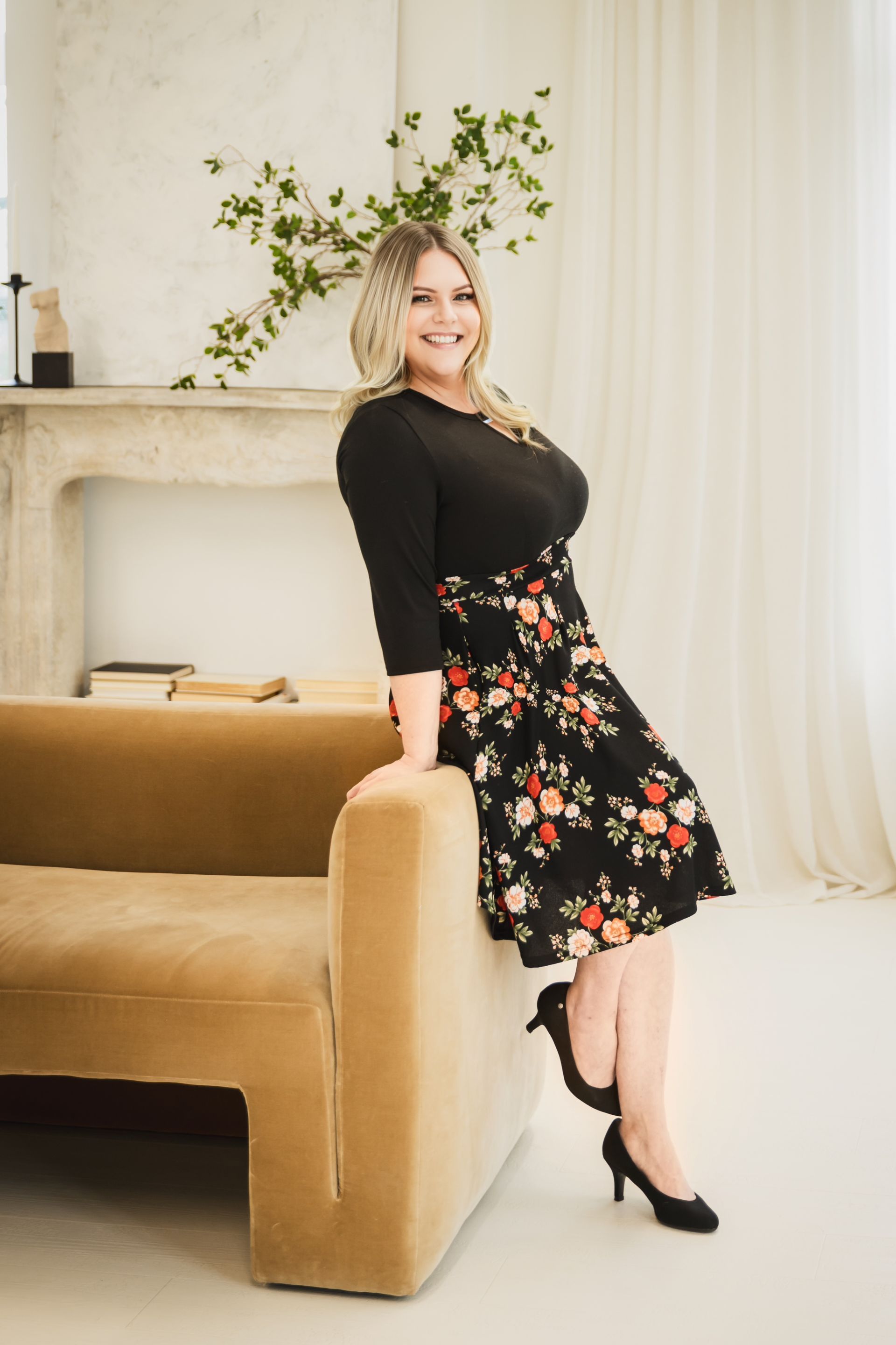 A woman in a black dress is leaning on a couch.