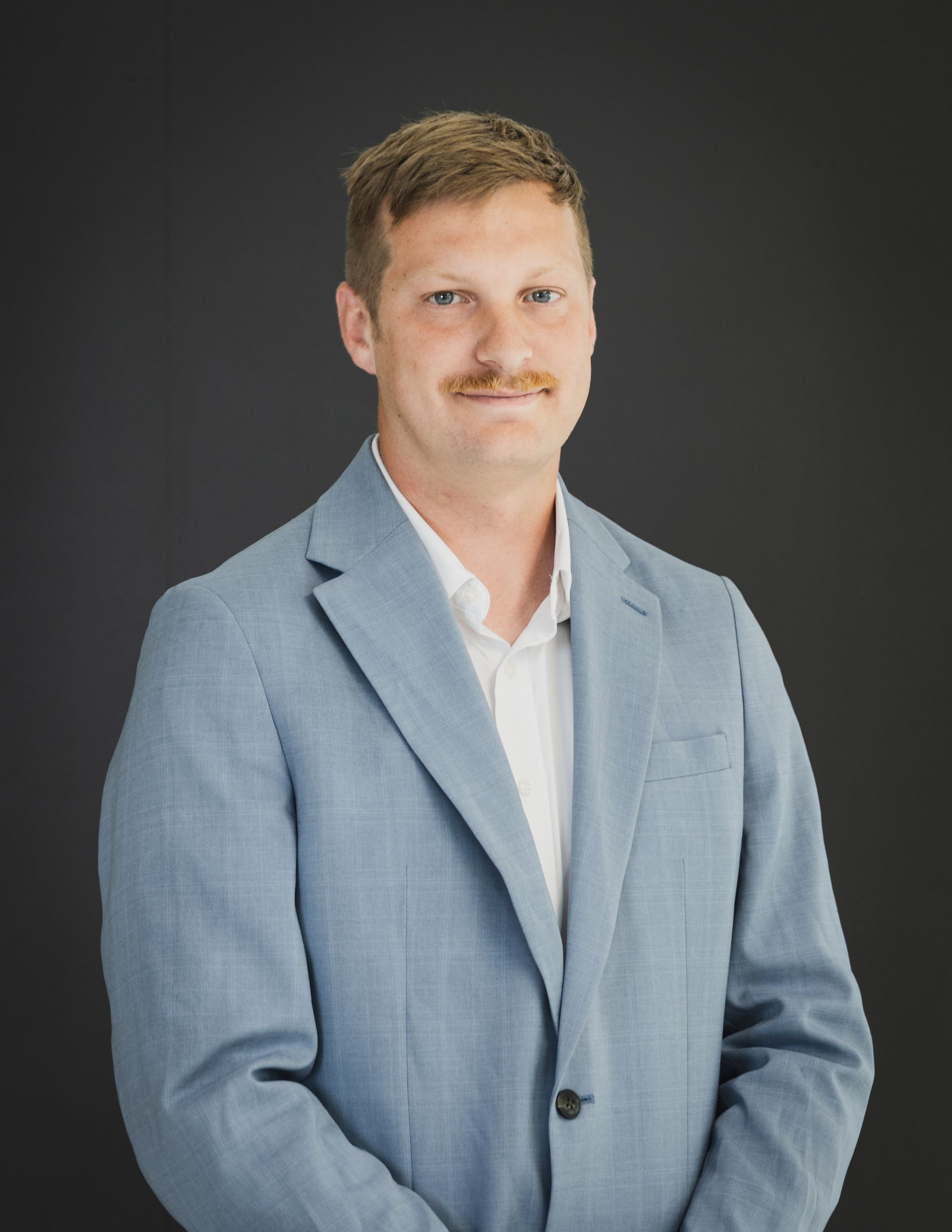 A man with a mustache is standing in front of a white railing.