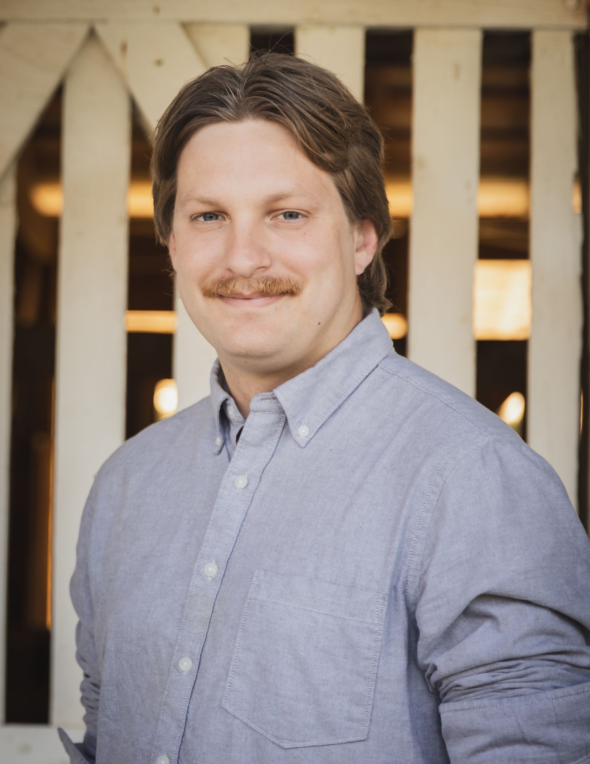 A man with a mustache is standing in front of a white railing.