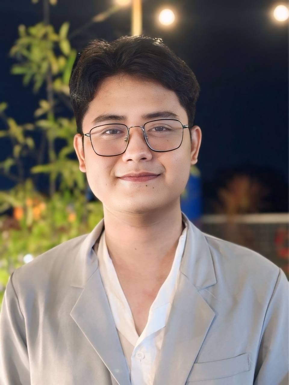 A young man wearing glasses and a suit is smiling for the camera.