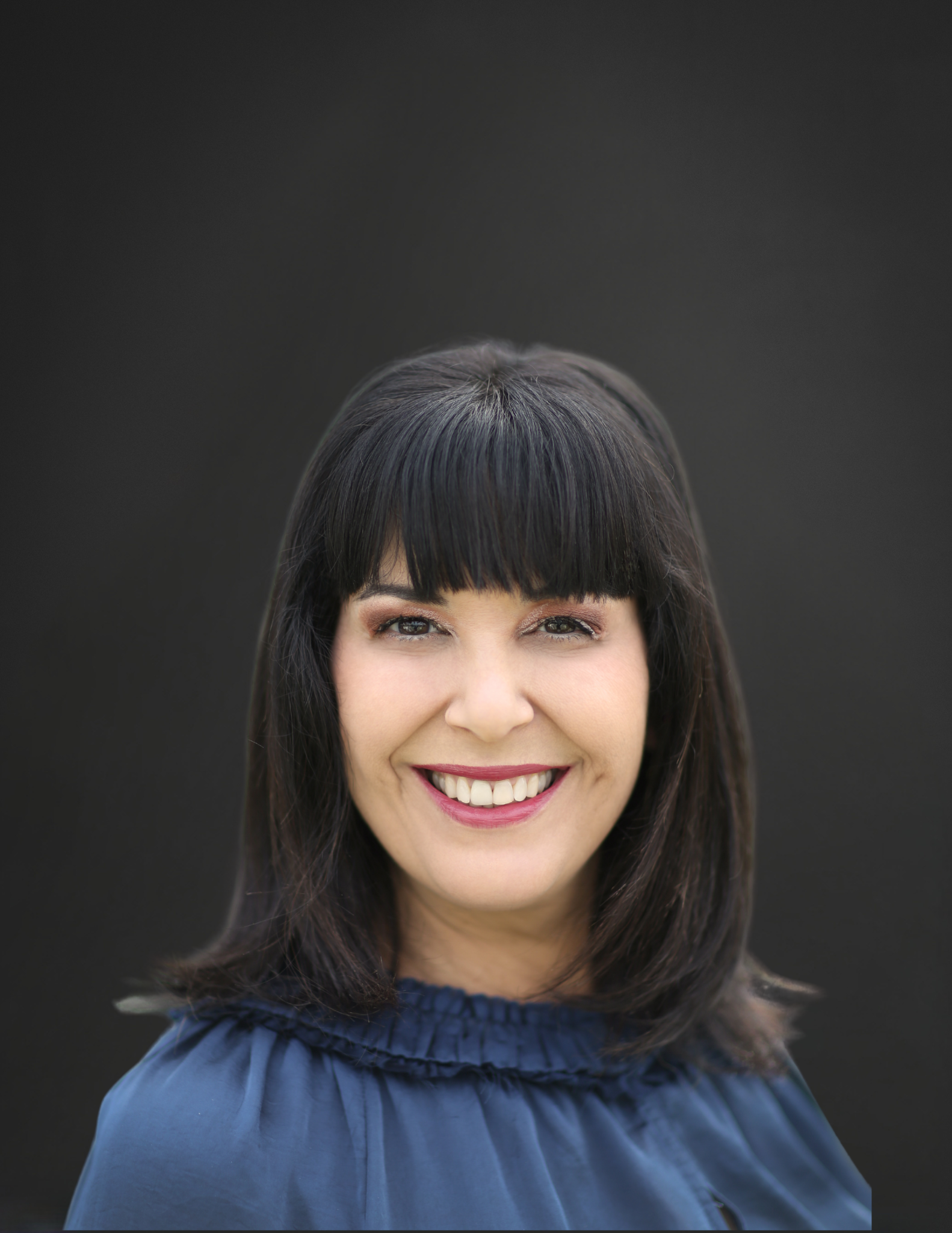 A woman with dark hair and bangs is smiling in a circle
