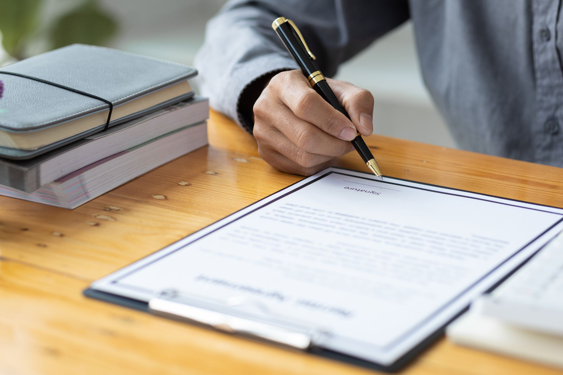 A person is signing a document on a clipboard with a pen.