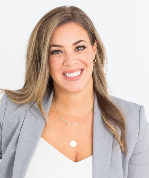 A woman wearing a gray jacket and a white shirt is smiling for the camera.