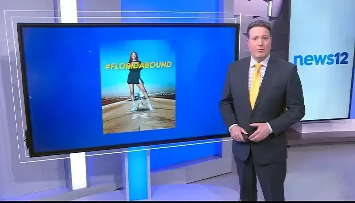 A man in a suit and tie is standing in front of a screen that says news12