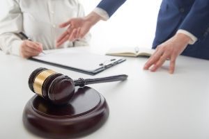 A woman is sitting at a table with a clipboard and a judge 's gavel.