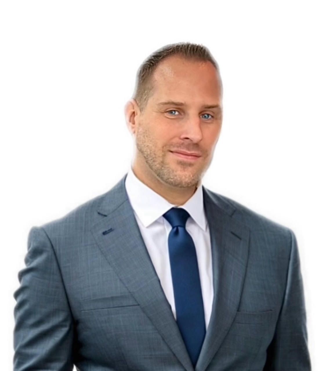 A man in a suit and tie is standing in front of a white background.