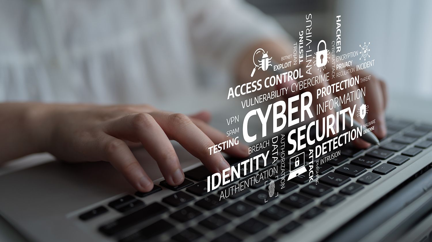 Hands typing on a laptop with cybersecurity keywords overlayed across the keyboard.