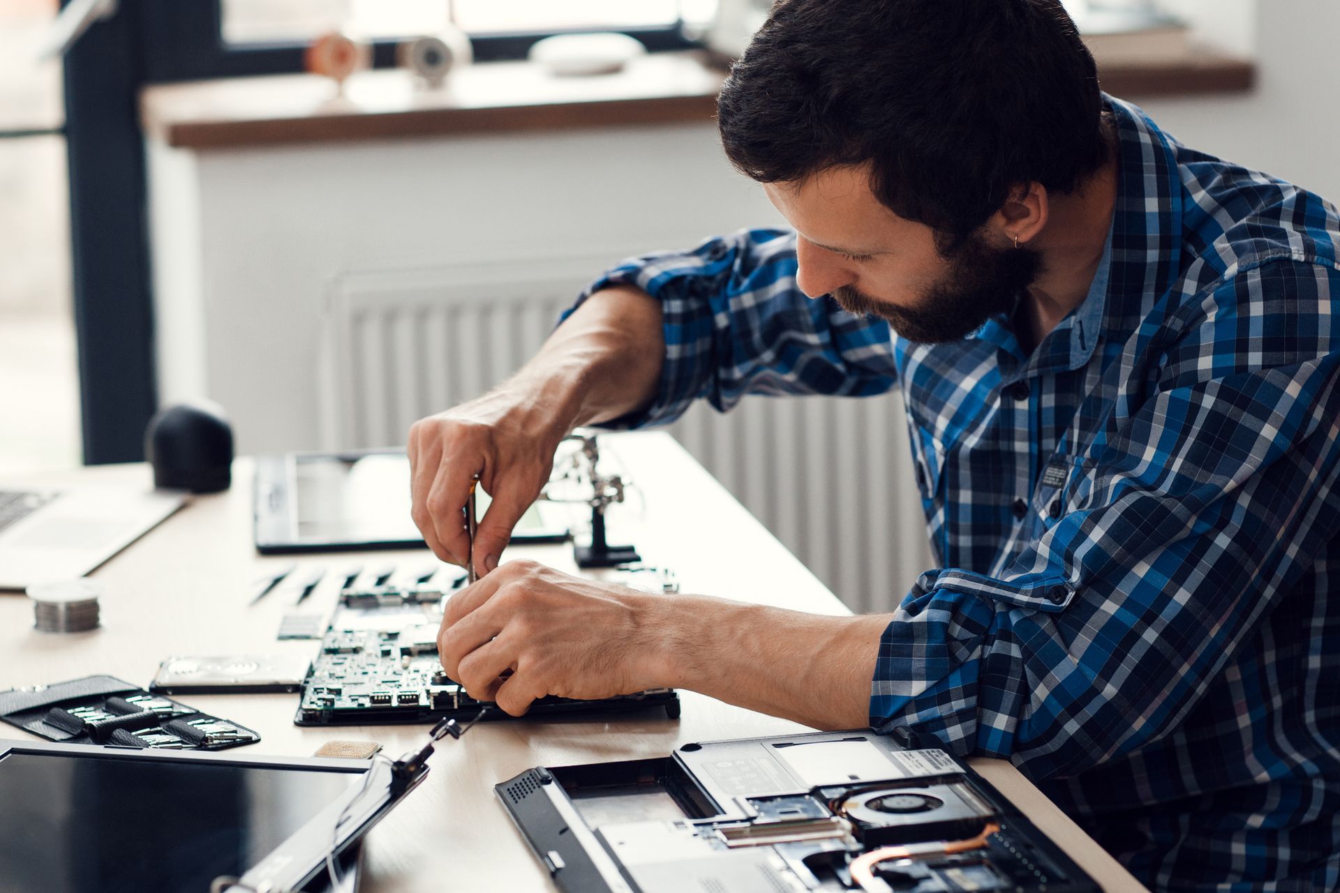 Side view showcasing computer repair with laptop disassembly using screwdriver on desk.