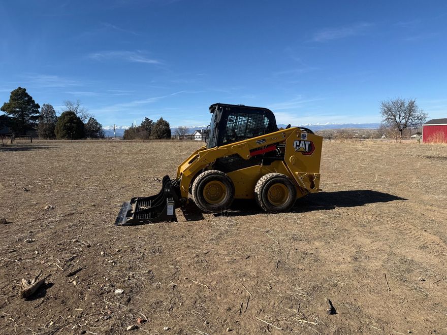 A yellow Caterpillar skid-steer loader sits on a dry, dirt field under a bright blue sky.