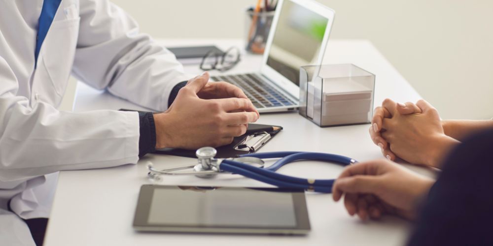 A doctor is sitting at a desk talking to a patient.
