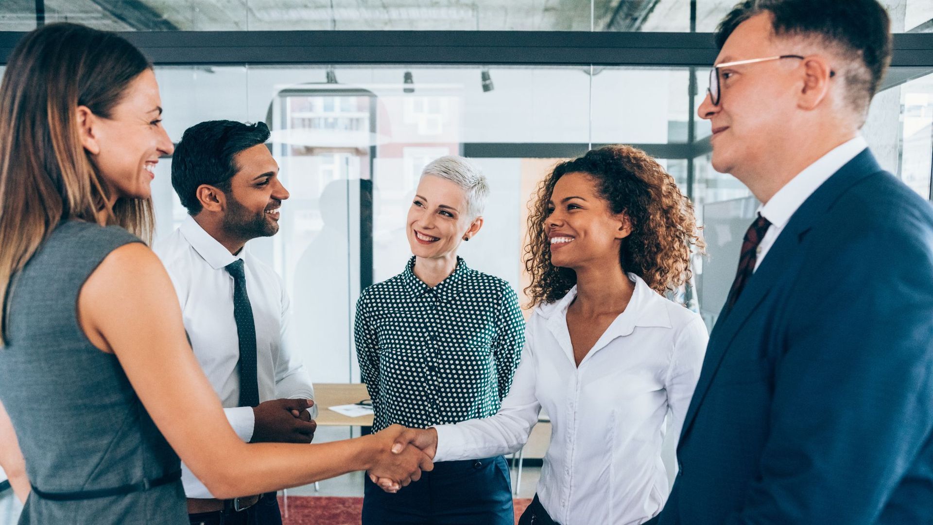 Colleagues shaking hands in a bright office conference room with a presentation board in the background