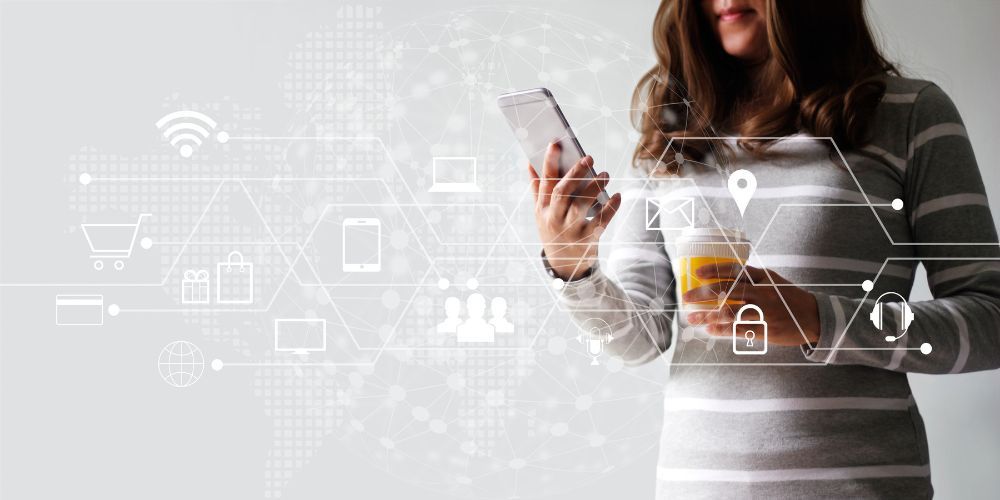 A woman is holding a glass of orange juice and using a smart phone.