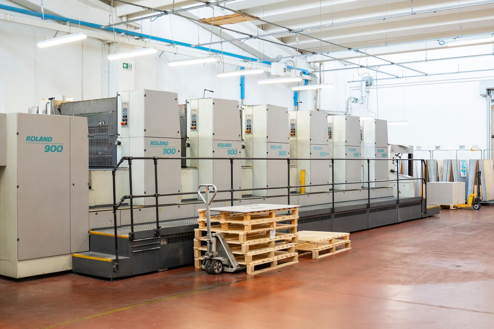 Linea di stampa industriale in una fabbrica luminosa, con pallet impilati e attrezzature all'interno.
