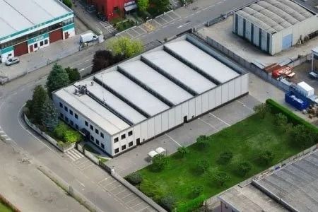 Vista aerea di un magazzino bianco accanto a un terreno vuoto e ad altri edifici industriali.
