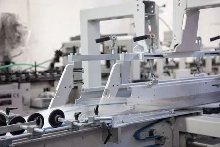 Macchinario industriale con rulli e bracci metallici in un luminoso ambiente di fabbrica.