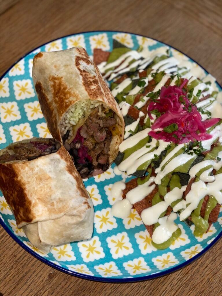 A plate of food with a burrito and enchiladas on a wooden table.