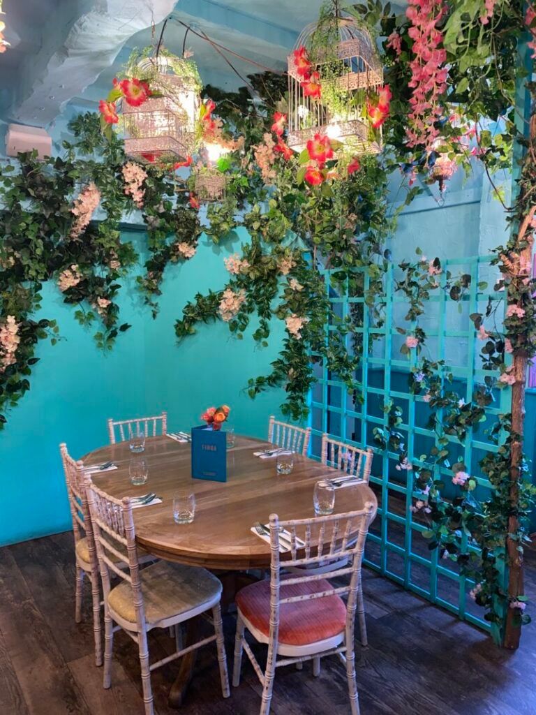 A dining room with a table and chairs and flowers hanging from the ceiling.