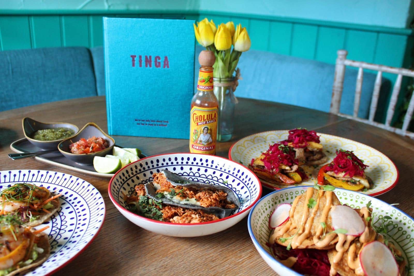 A table topped with plates of food and a bottle of hot sauce.
