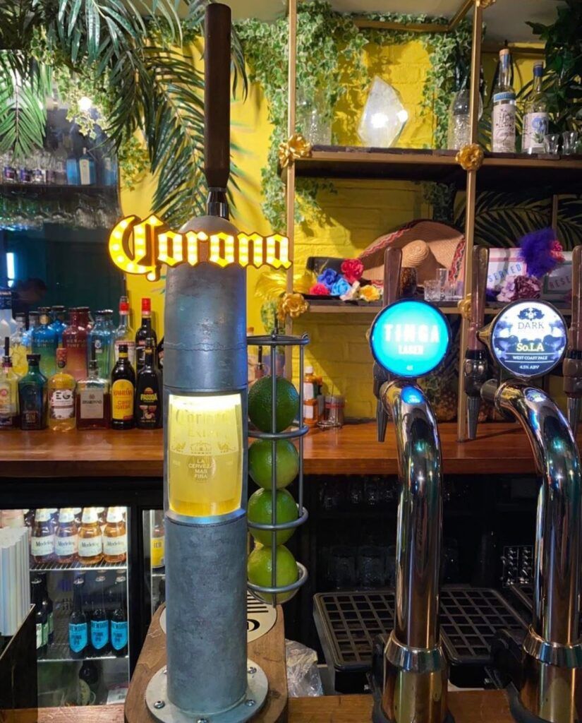 A corona beer dispenser is sitting on a bar.