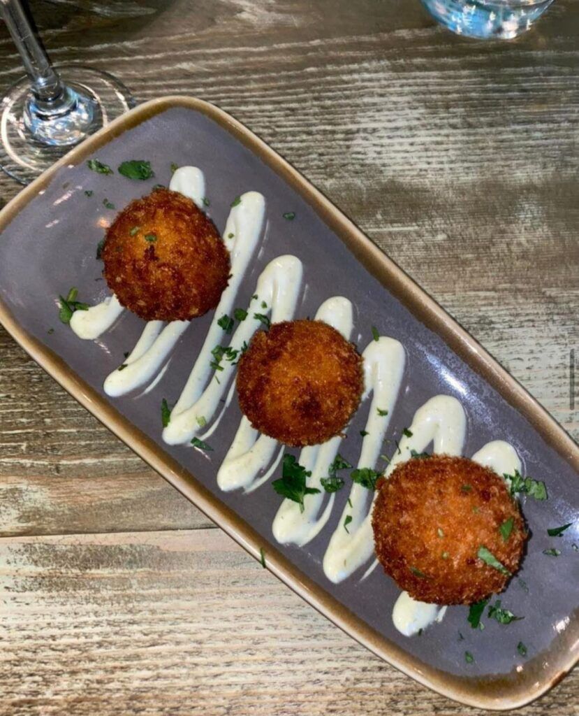 A plate of food on a wooden table with a glass of wine in the background