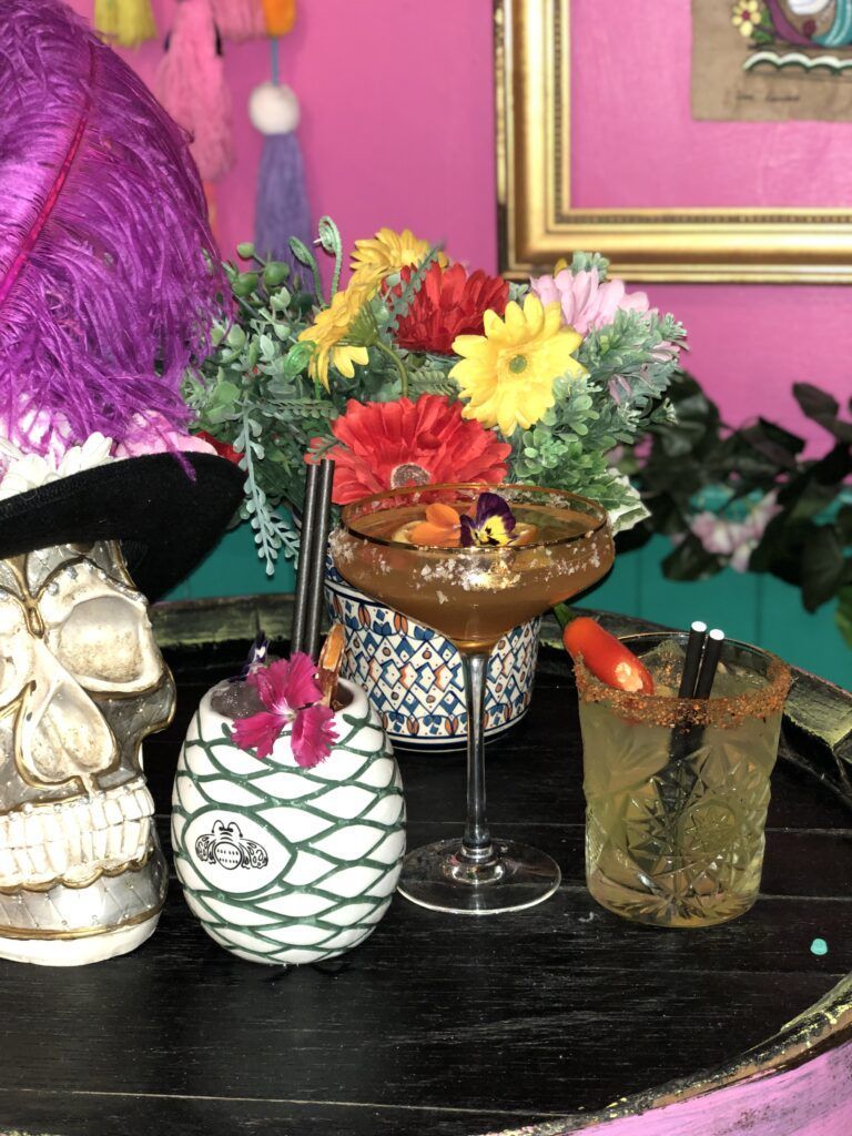A table with a vase of flowers and two drinks on it.