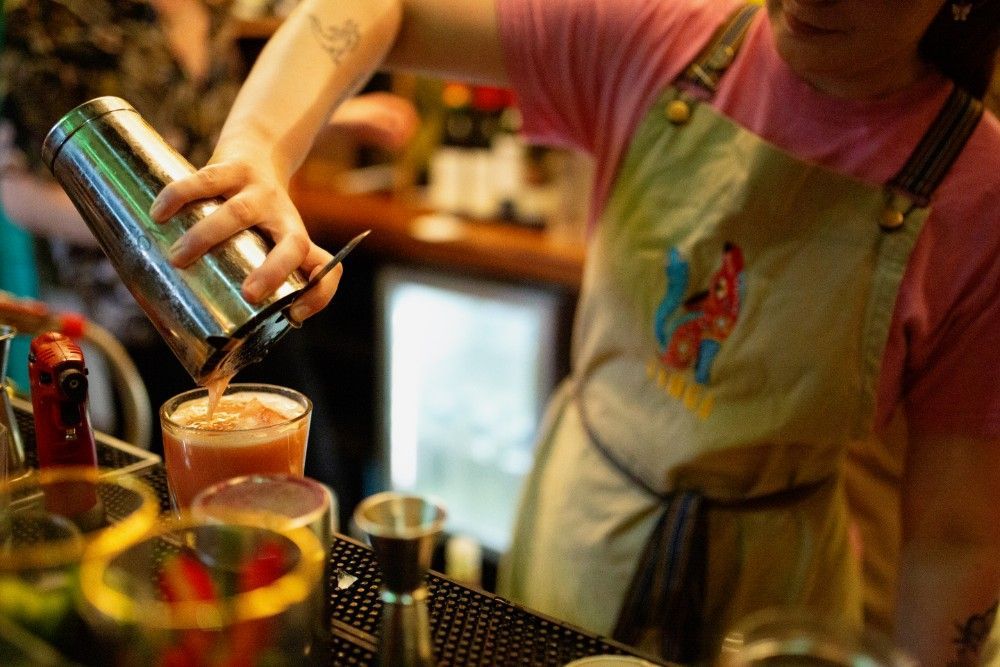 A bartender is pouring a drink from a shaker into a glass.