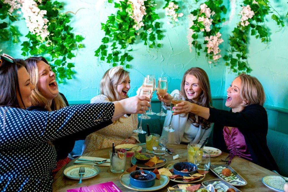 A group of women are sitting at a table toasting with champagne glasses.