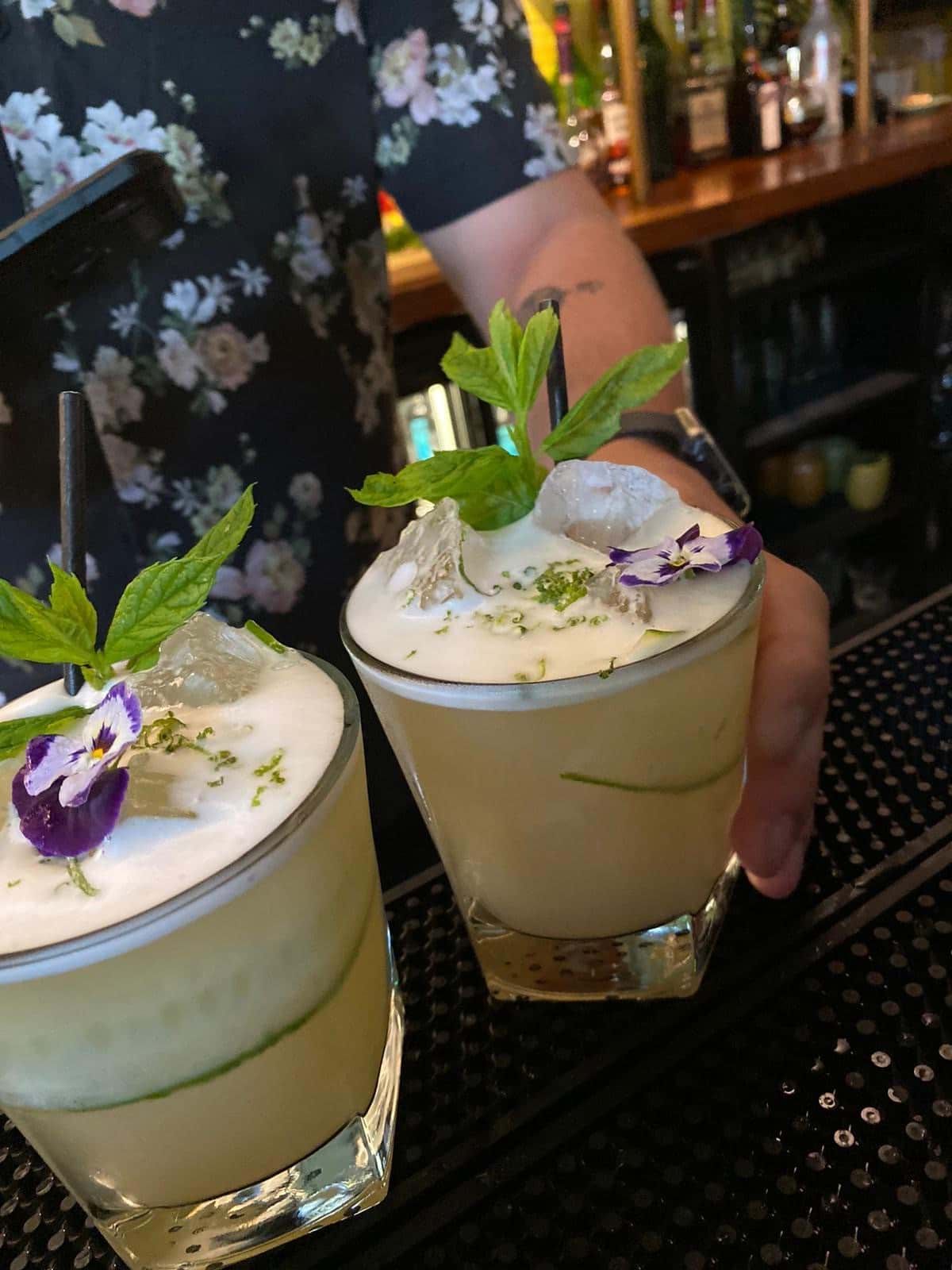 A person is holding two drinks with flowers on top of them.