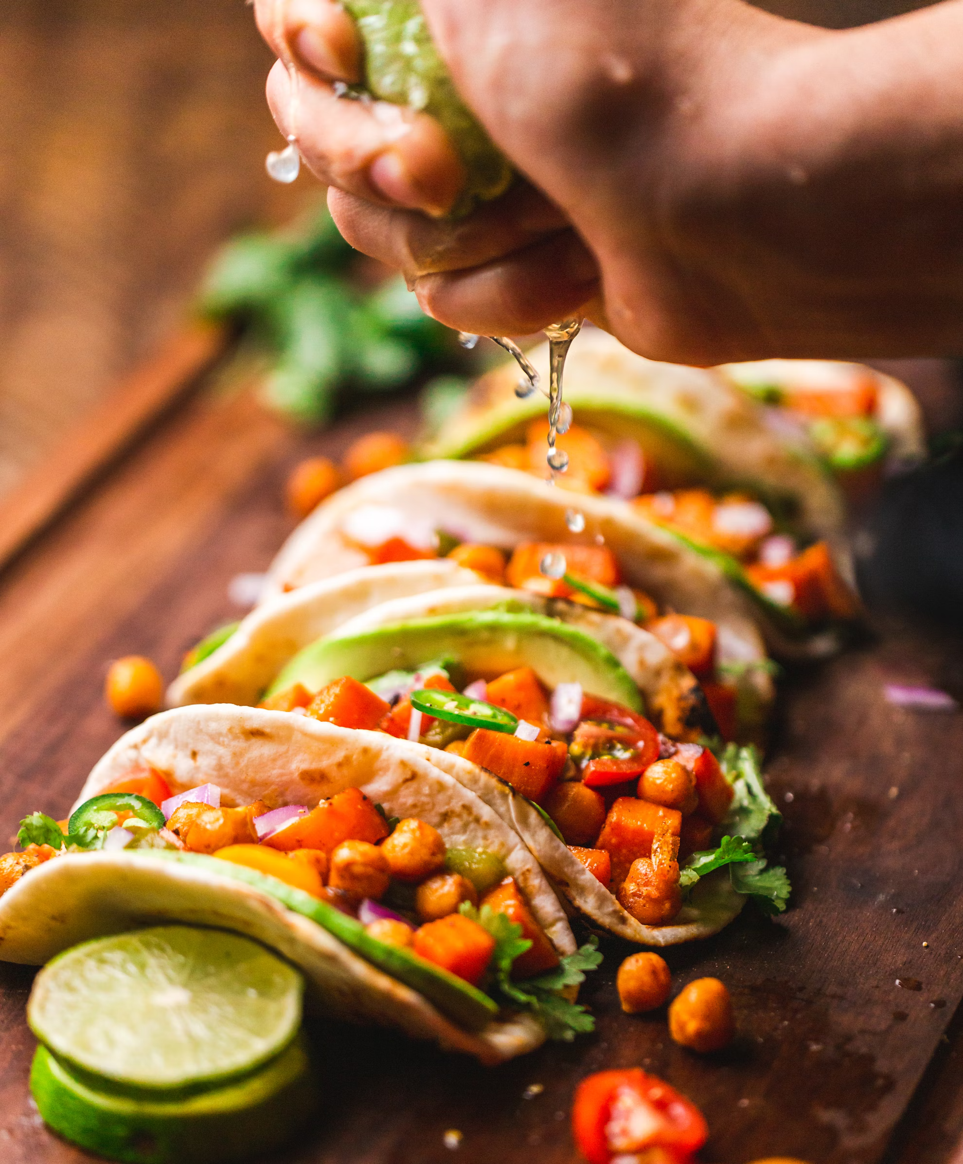 A person is squeezing lime juice on a taco on a cutting board.