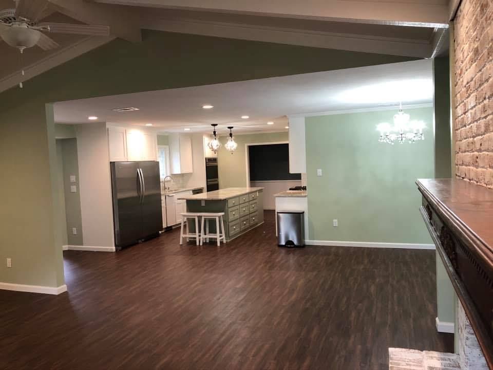 A living room with hardwood floors and a kitchen in the background.