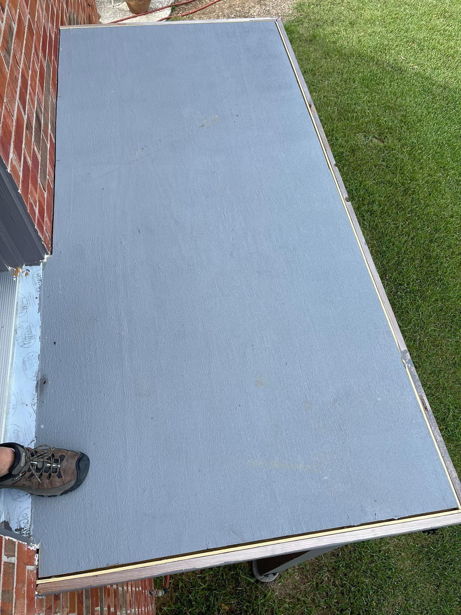 A person is standing on a carpeted porch next to a brick wall.