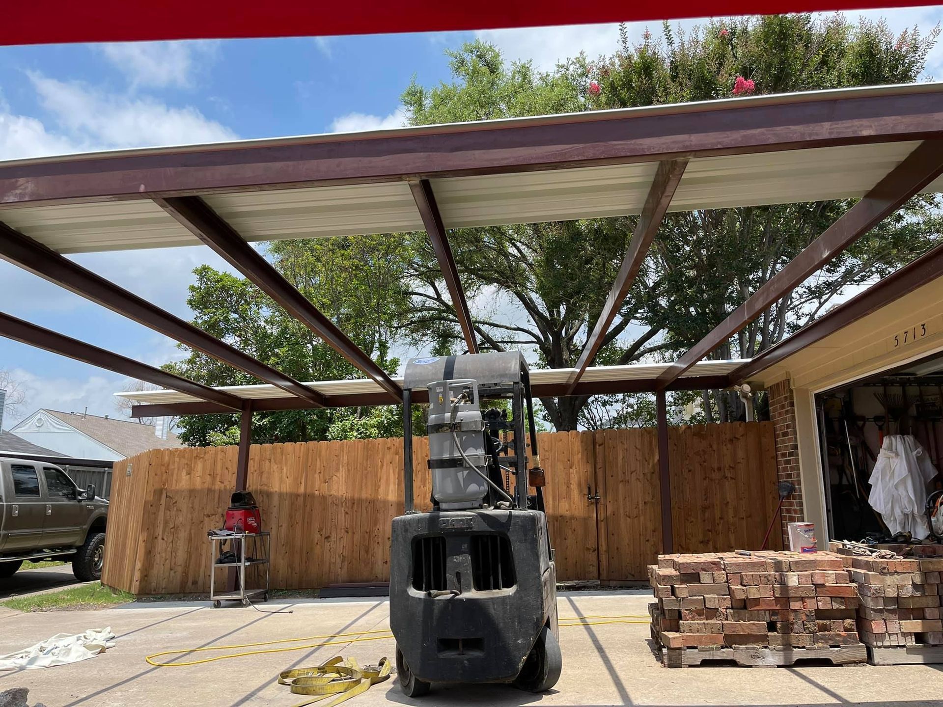 A forklift is sitting under a roof in a driveway.