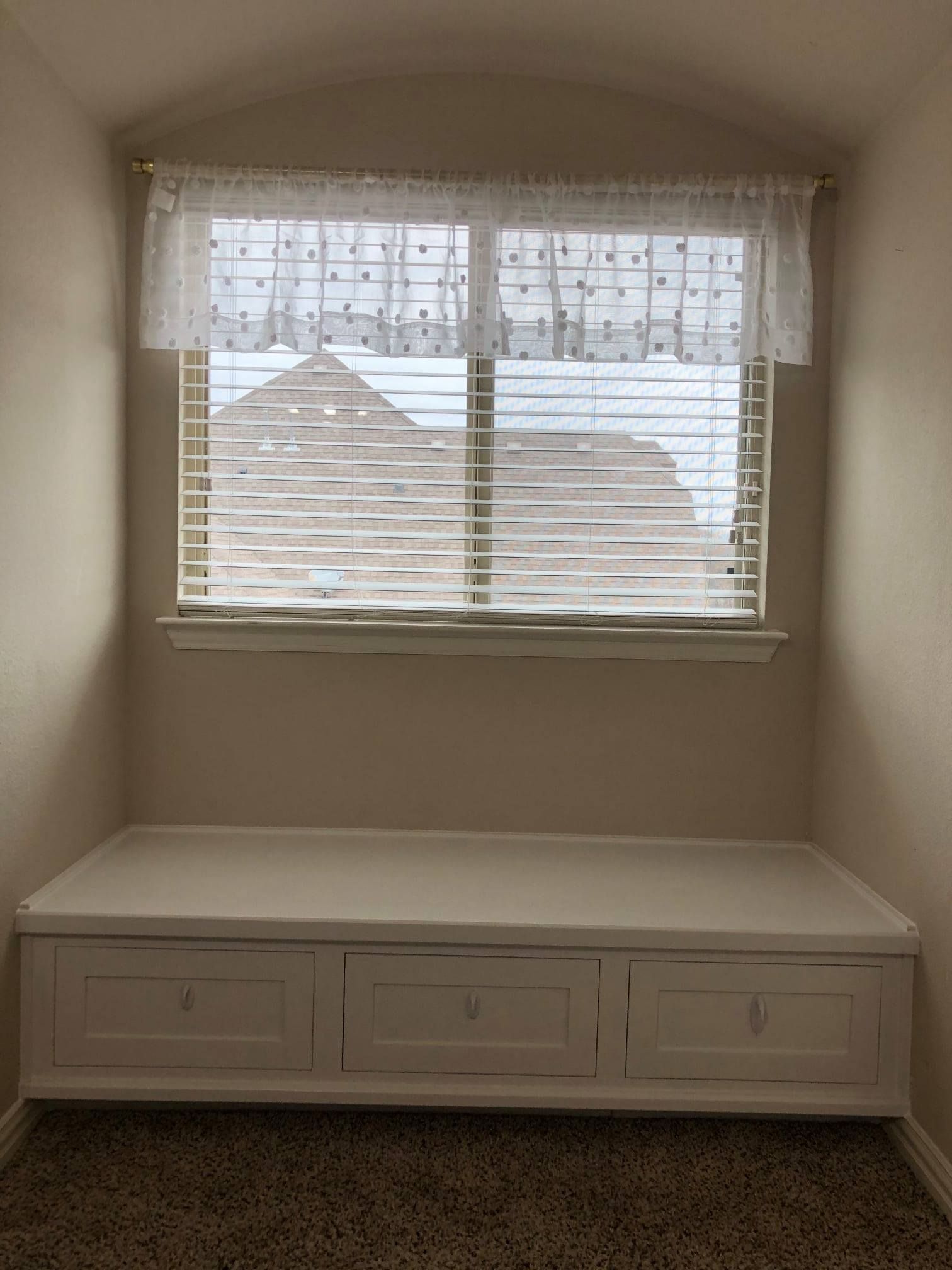 There is a window with blinds and a bench in the corner of the room.