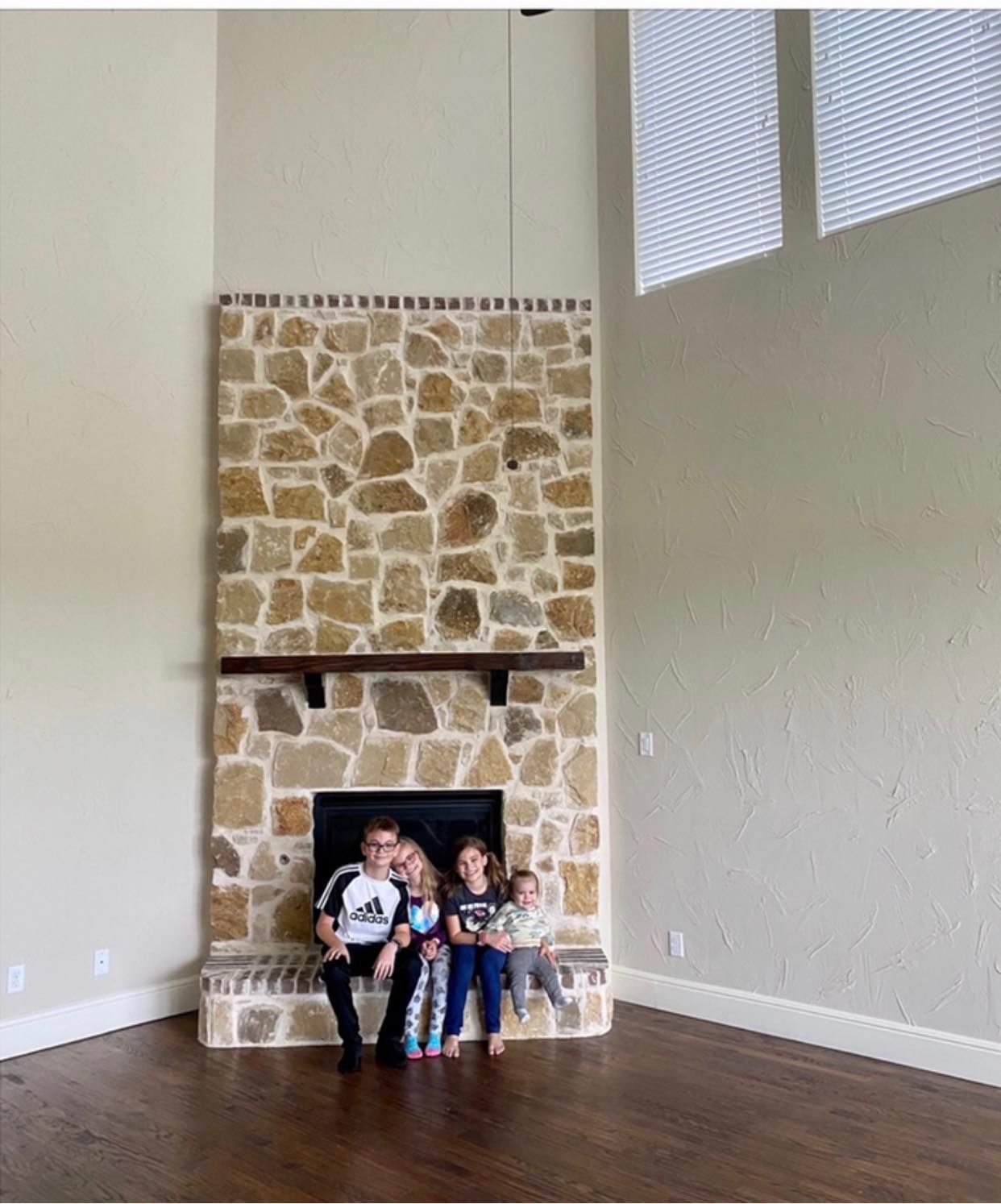 A family is sitting in front of a stone fireplace in an empty room.