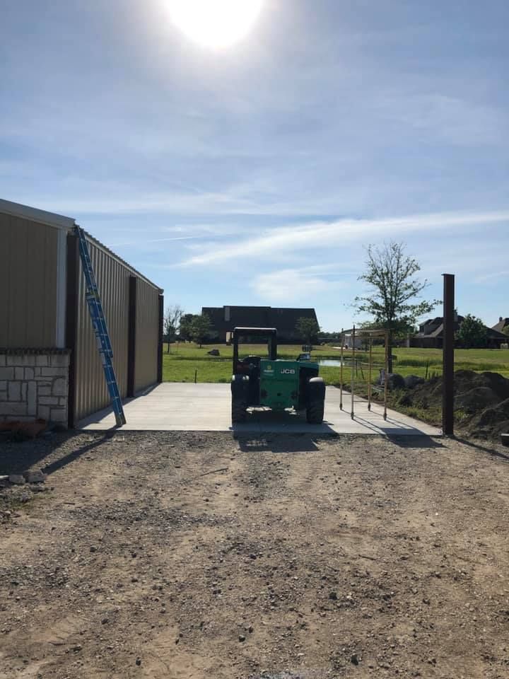 A green tractor is parked in a dirt lot in front of a building.