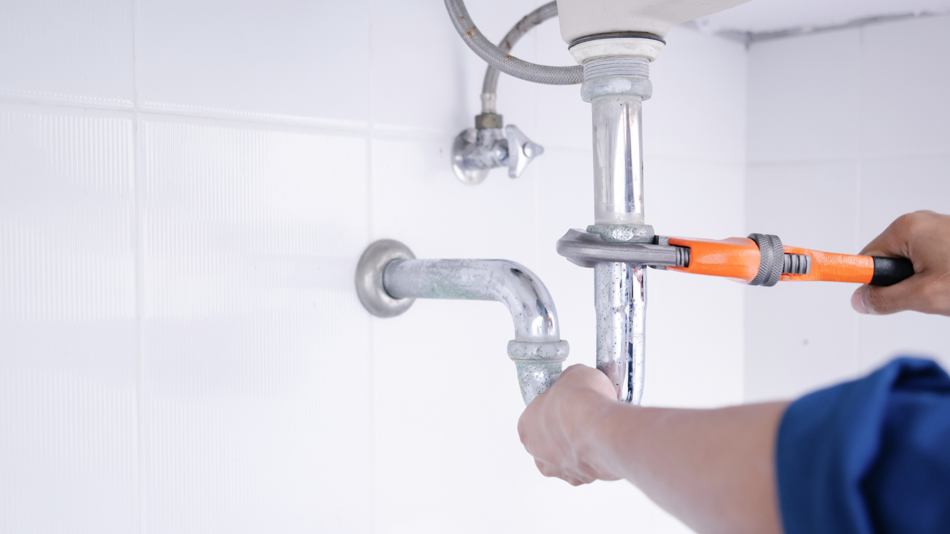 A plumber is fixing a sink pipe with a wrench.