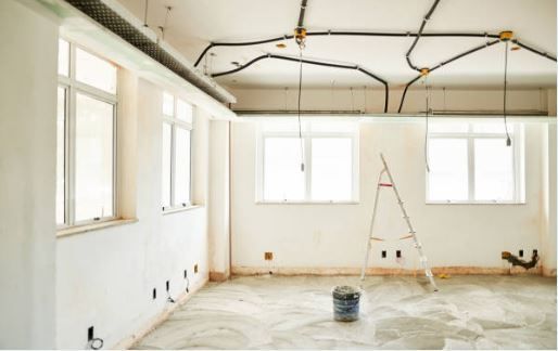 An empty room with a ladder and a bucket on the floor.