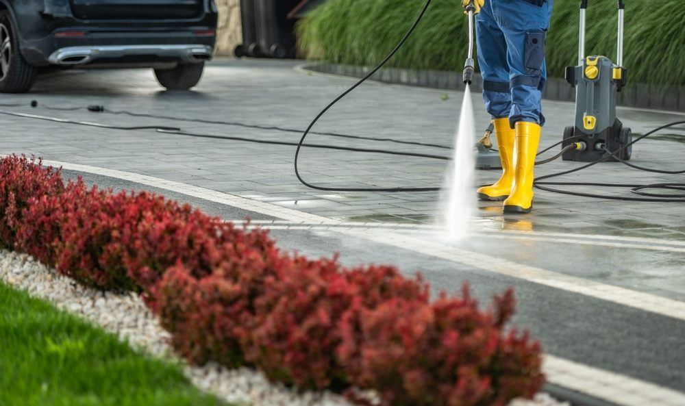 AllTex Home & Commercial Services Caucasian Man Cleaning His Modern House Surrounded by a Powerful Pressure Washer. Washing a Brick-Made Driveway.