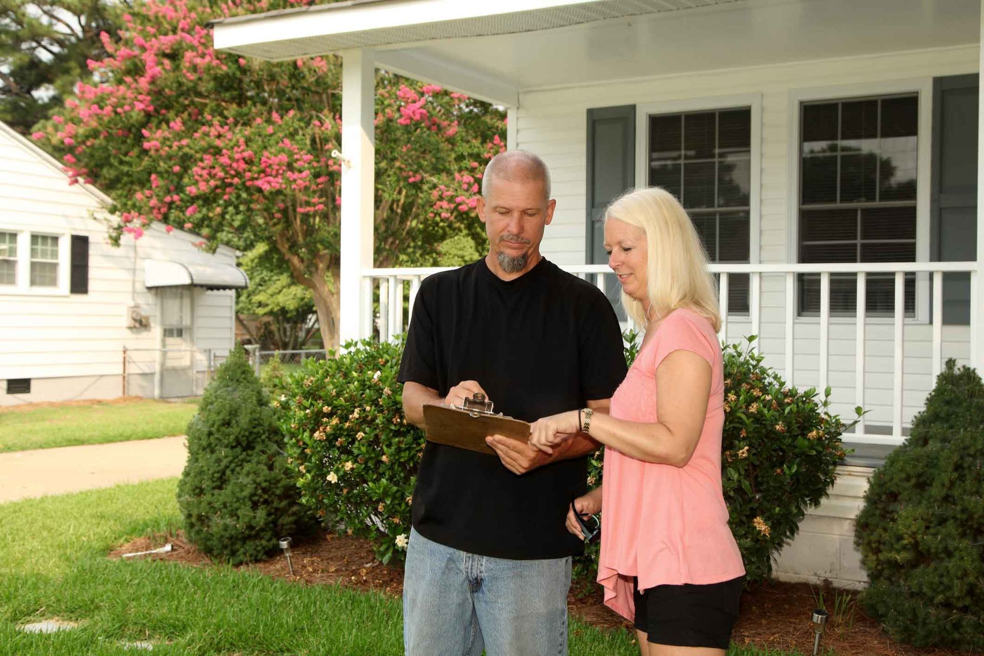 A man and a woman are standing in front of a house looking at a clipboard.
